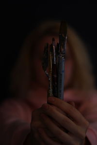 Woman holding paintbrushes against black background