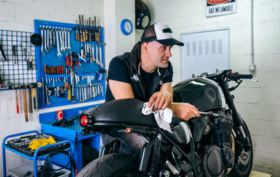 Man holding tool while leaning on motorcycle in garage