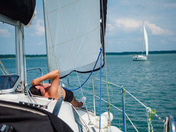 Young person sunbathing on a sailboat under the sail