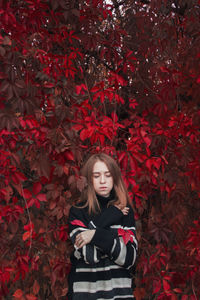 Autumn portrait of a beautiful cute woman against a background of bright red leaves. black sweater
