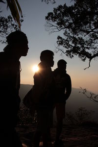 Silhouette couple standing by tree against sky during sunset
