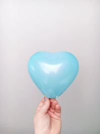 Close-up of hand holding heart shape balloon against white background