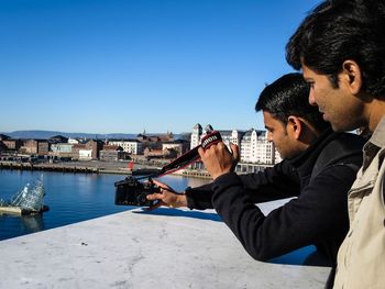 Side view of man photographing with camera against sky