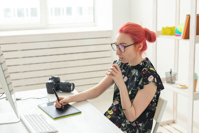 Young woman looking away while sitting on table at home