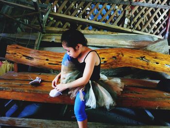 Full length of girl wearing shoe while sitting on wooden bench