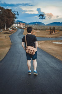 Rear view of man walking on country road along trees