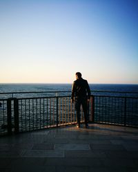 Rear view of man standing on pier over sea against sky