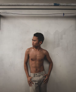 Young man looking away while standing against wall