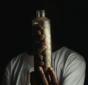 Close-up of man holding walnuts in bottle against black background