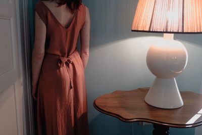 Midsection of woman standing by illuminated lamp on table at home