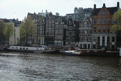 Boats in river by cityscape against sky