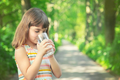 Cute girl drinking water while standing outdoors