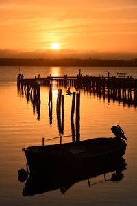 Silhouette wooden posts in sea against sky during sunset