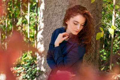 Woman with red curly hair poses on the street through yellow leaves, autumn mood . vertical photo