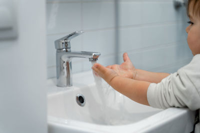 Toddler washing hands in sink at home