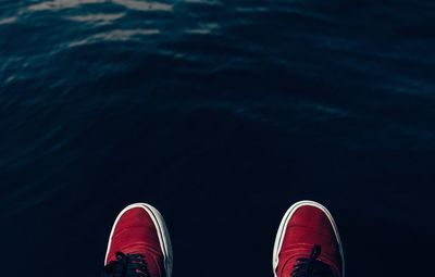 Close-up of cropped shoes against calm water