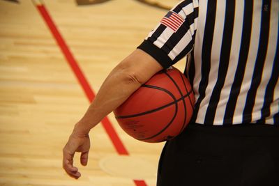 Midsection of referee with basketball standing in court