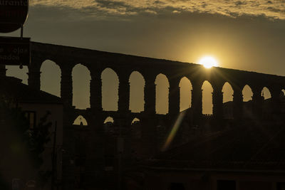 Arch bridge by building against sky during sunset