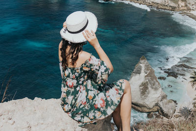 High angle view of woman sitting on rock by sea