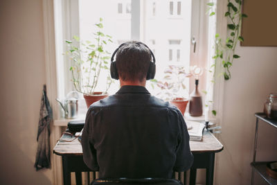 Rear view of male entrepreneur listening music through headphones sitting at home office