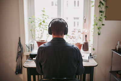 Rear view of male entrepreneur listening music through headphones sitting at home office