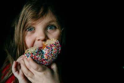 Portrait of girl eating food against black background