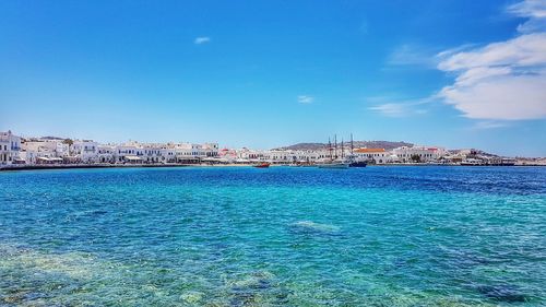 Sea by cityscape against blue sky