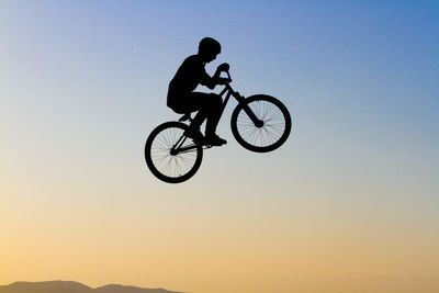 Man riding bicycle against sky during sunset