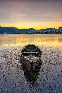 Boat moored in lake against sky during sunset