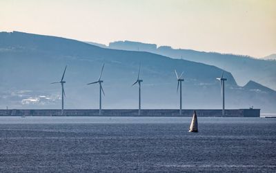 Windmills by sea against mountain