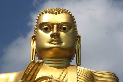 Low angle view of golden buddha statue against sky