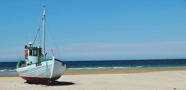 Boat moored on beach against clear sky