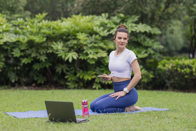Young caucasian woman exercising online in summer park during covid-19 coronavirus pandemic.