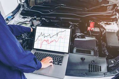 Midsection of mechanic using laptop on car