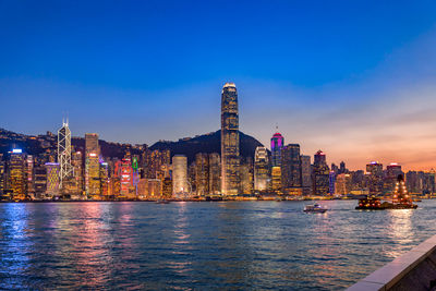 Illuminated buildings by river against sky in city