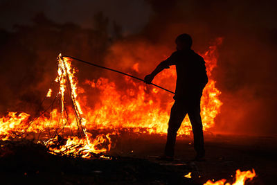 Silhouette man holding burning rope with stick at field