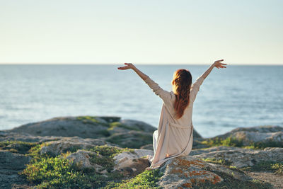 Rear view of woman on rock by sea against clear sky