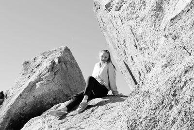 Low angle portrait of young woman sitting on rock formation