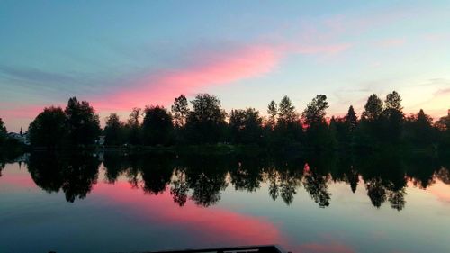 Reflection of trees in calm lake at sunset