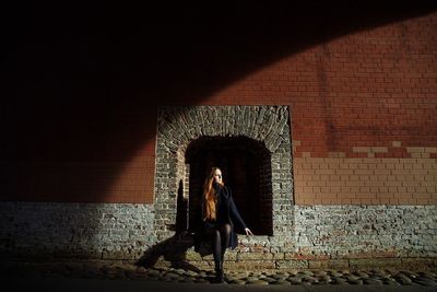 Full length of woman standing against brick wall