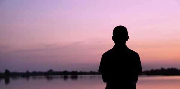 Silhouette man standing by lake against sky during sunset