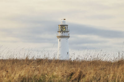 Lighthouse on field against sky