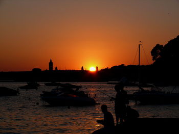 Silhouette boats moored at harbor against clear sky during sunset