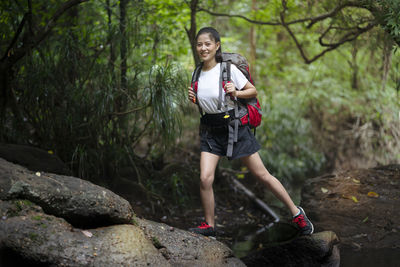 Full length of smiling young woman on rock in forest