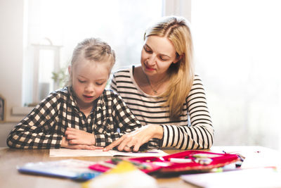 Girl studying while sitting with mother at home