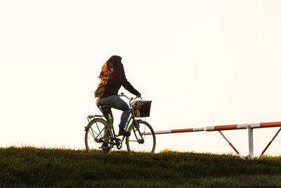 Man riding bicycle on field against clear sky