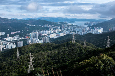 Electricity pylons by trees in city against sky