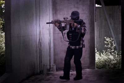 Full length of man holding rifle standing by wall outdoors