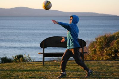 Side view of boy playing soccer on field with lake in background