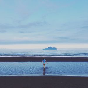 Rear view of boy standing on beach against sky